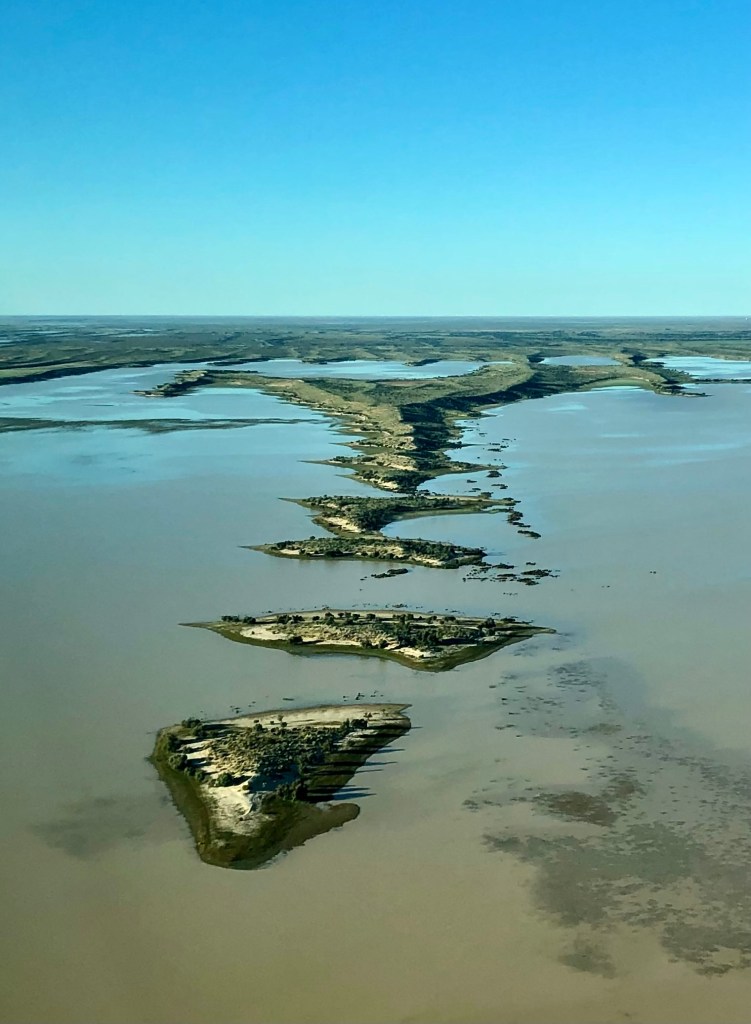 Aerial view of Kati Thanda South, showcasing elongated land formations surrounded by water under a clear blue sky.