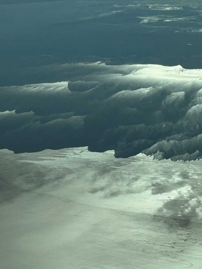Aerial view of reflective water surface with clouds casting shadows, showcasing the textures and patterns of the landscape below.