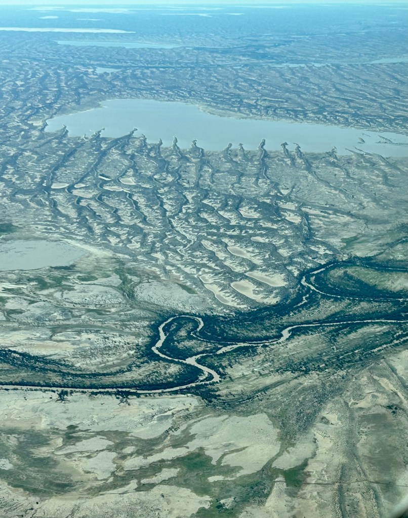 Aerial view of a vast, textured landscape featuring winding rivers and patches of water, with dry areas and unique formations evident.