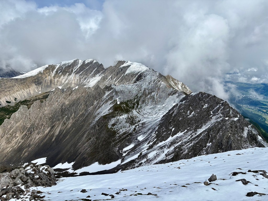 A panoramic view of rugged snow-capped mountain peaks under a cloudy sky.