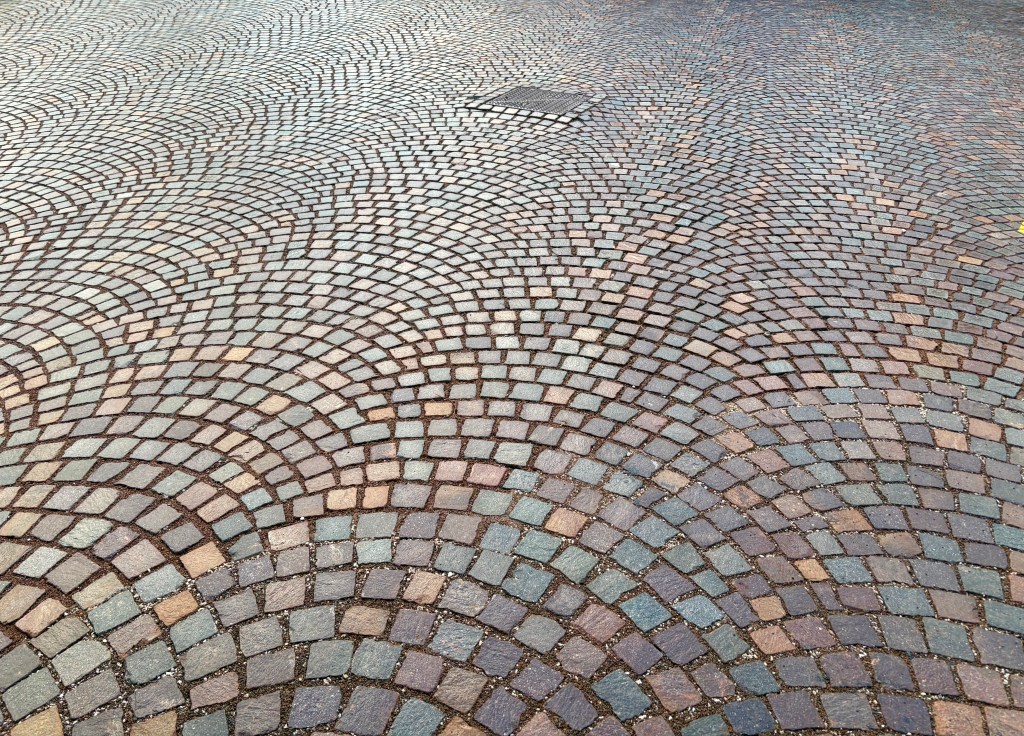 A close-up view of a textured cobblestone pavement featuring curved patterns and various shades of stones.