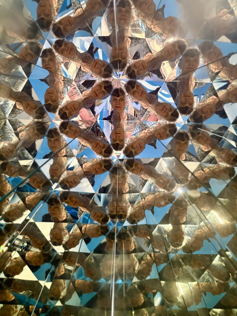 A kaleidoscopic view featuring multiple mirrored reflections of a woman's face against a blue sky backdrop.