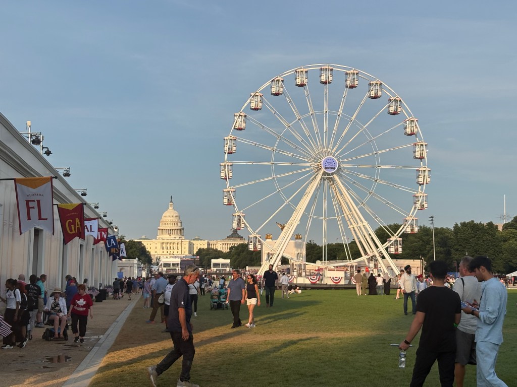A Ferris wheel at an outdoor event with the U.S. Capitol building in the background, surrounded by people enjoying the festivities.